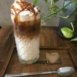 Indulge in a clear glass of cappuccino, elegantly crowned with a swirl of luscious whipped cream and drizzled with rich caramel sauce.